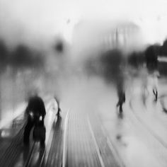 blurry photograph of people walking down the street on a rainy day in black and white