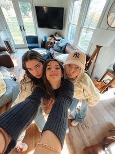 three girls are standing in the middle of a living room with their arms around each other