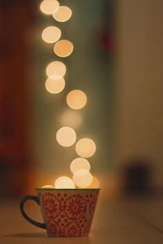 a red and white coffee cup sitting on top of a table with lights in the background