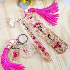 two key chains with pink tassels on top of a wooden table next to flowers