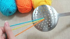 a person holding a ball of yarn and a metal strainer with knitting needles in it