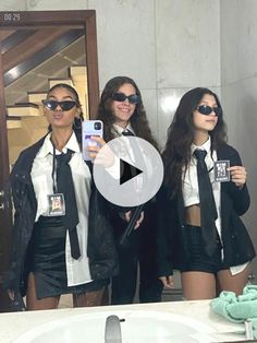 three women in suits and ties are taking a selfie with their cell phones as they stand in front of a bathroom mirror