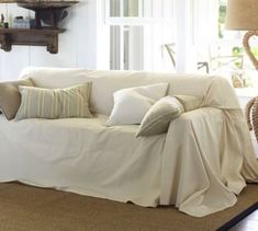 a living room with a couch covered in white sheets and pillows on the floor next to a lamp