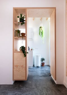 an open door leading to a bathroom with potted plants on the shelves and a toilet