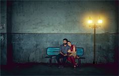 a man and woman sitting on a bench in front of a street light at night