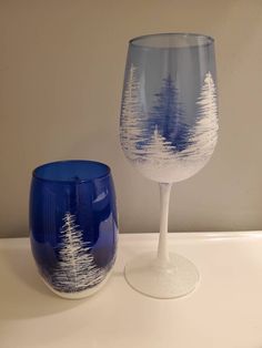 two wine glasses sitting next to each other on top of a white table with trees painted on them