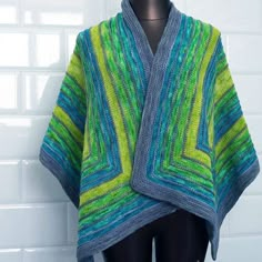 a green and blue knitted shawl sitting on top of a mannequin