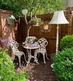 a table and chairs in a garden with flowers on the ground next to a fence