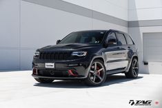 a black jeep is parked in front of a white building with red rims on it