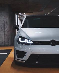 a white volkswagen car parked in a parking garage with its lights on and it's hood up