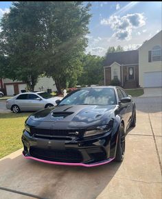 a black sports car parked in front of a house with pink stripes on the side