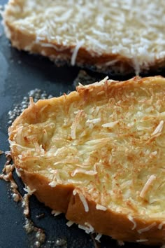 two pieces of bread with cheese and coconut toppings on them sitting on a black surface