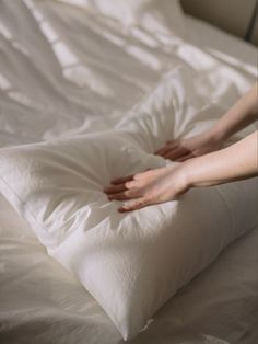 a person reaching for pillows on top of a bed