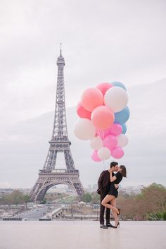 a couple kissing in front of the eiffel tower with pink and blue balloons