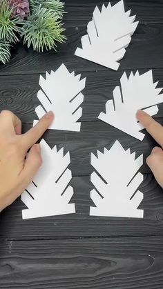 someone is making paper snowflakes out of white paper on a wooden table with pine branches