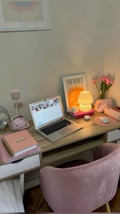 a laptop computer sitting on top of a desk next to a pink chair and lamp