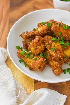 a white plate topped with chicken wings covered in sauce and garnished with green onions