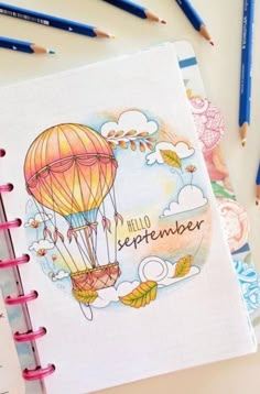 a notebook with an image of a hot air balloon on it and some pencils next to it