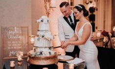 a bride and groom cutting their wedding cake together at the reception table in front of candles