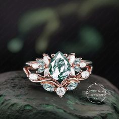 a green and white diamond ring sitting on top of a rock with leaves around it