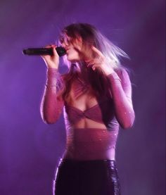 a woman with long hair is holding a microphone in her hand and singing into the microphone