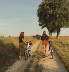 two women walking down a dirt road with bicycles