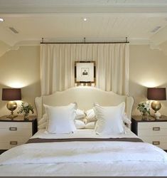 a bed with white sheets and pillows in a bedroom next to two lamps on either side of the bed