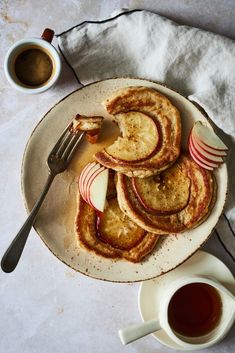 pancakes with apple slices and syrup are on a plate next to a cup of tea