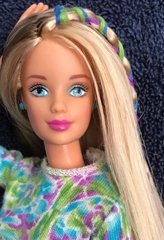 a doll with blonde hair and blue eyes wearing a multicolored sweater on a blue background