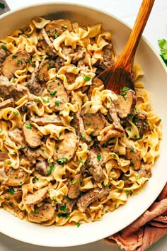 a white bowl filled with pasta and meat on top of a wooden spoon next to parsley