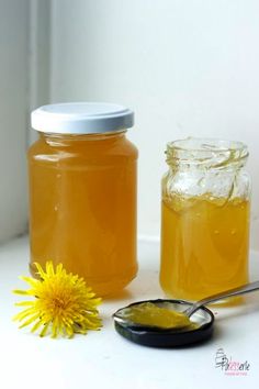 two jars filled with honey sitting next to a dandelion