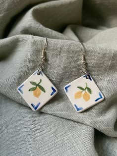 a pair of earrings with lemons painted on them sitting on a piece of cloth