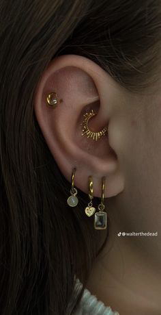 a woman wearing gold ear piercings with two small charms on her left ear, and one