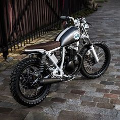 a black and white motorcycle parked on the side of a brick road next to a fence