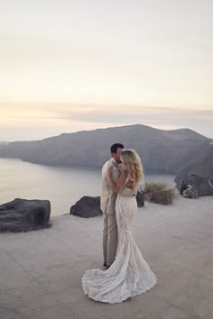 a man and woman standing next to each other on top of a hill near the ocean