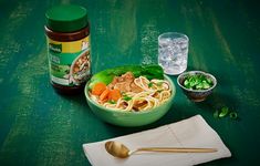 a green bowl filled with noodles and vegetables next to a jar of peanut butter on a table