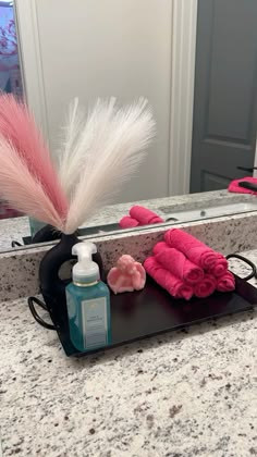 a bathroom counter with towels, soap and pink feathers