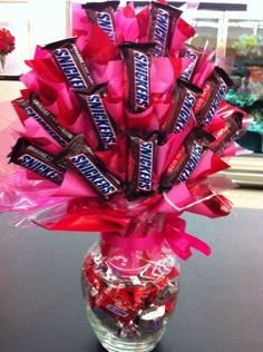 a vase filled with candy bars and wrapped in pink ribbon