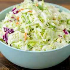 a blue bowl filled with coleslaw on top of a wooden table