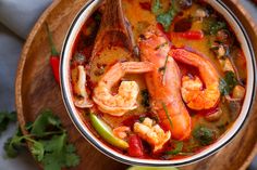 a bowl filled with shrimp and vegetables on top of a wooden plate next to cilantro