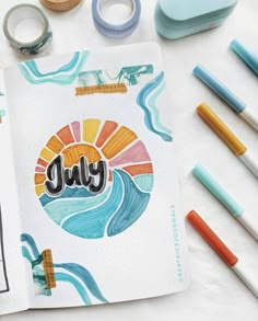 an open notebook with the word july written on it next to markers, pens and washi tape