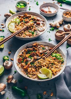 two bowls filled with noodles, mushrooms and limes next to chopsticks on a table