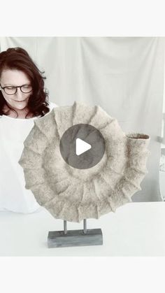 a woman sitting in front of a large object on top of a white table next to a curtain