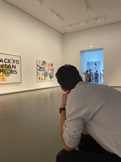 a man sitting on the ground looking at artwork in an art gallery with people standing around