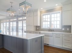 a large kitchen with white cabinets and an island in front of the sink is lit by pendant lights