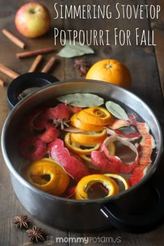 a pot filled with oranges and apples on top of a wooden table next to cinnamon sticks