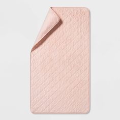 the pink quilted blanket is folded on top of a white surface with a light colored background