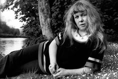 a woman laying on the ground next to a tree and some water with her hands in her pockets