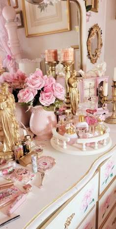 a dresser covered in pink roses and gold decorations with candles, perfume bottles and other items