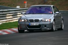 a silver car driving down a race track with people in the back seat looking on